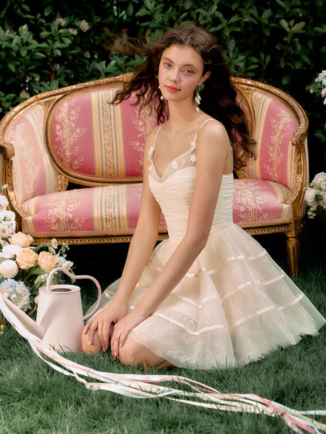 A model in a soft ivory tulle dress sits gracefully on the grass with trailing ribbons, surrounded by roses in a whimsical princesscore moment.