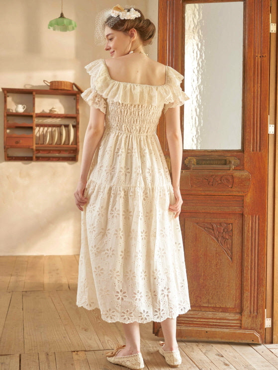 Back view of a woman in a cream off-shoulder eyelet dress, styled with a floral veil and ribbon shoes in a warm cottagecore setting.