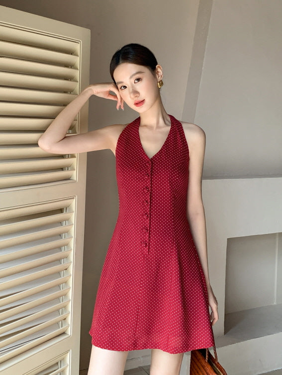 Model poses gracefully by a shuttered window in a cherry red halter dress with a flared hem, evoking a soft vintage summer outfit vibe.