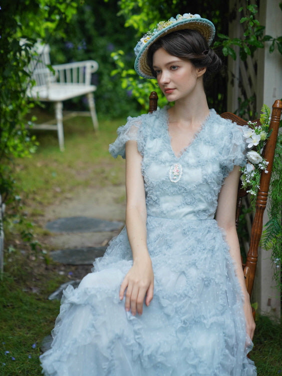 Seated in a floral archway, the model wears a delicate blue vintage-style dress and a flower-trimmed hat, capturing the essence of a dreamy princesscore afternoon.