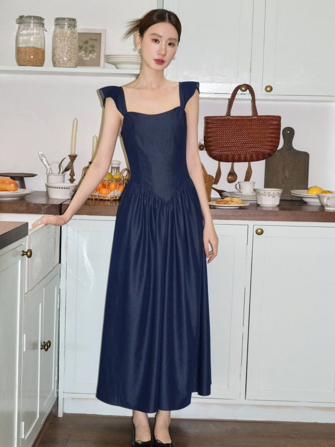 In a soft cottage-style kitchen, a woman wears a navy vintage-inspired dress with flutter straps and a fairytale charm, creating a refined look.