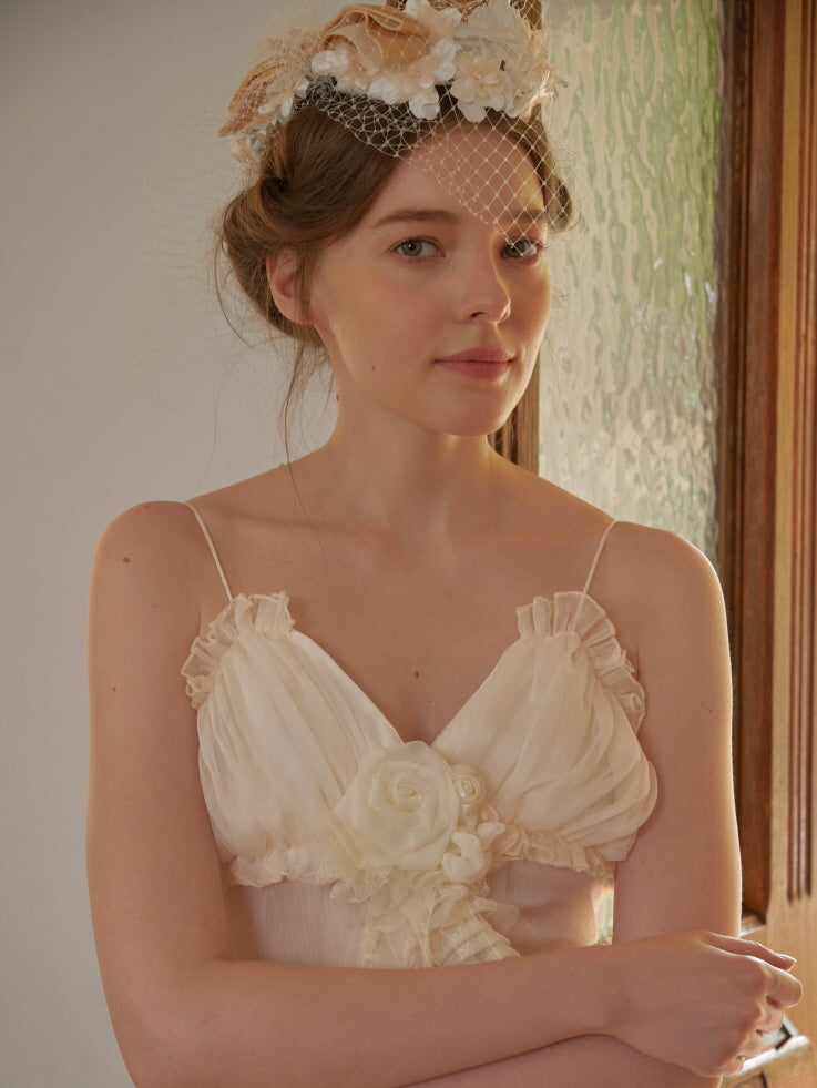 A woman poses with folded arms in a romantic cream tulle dress adorned with a rose applique, styled in a princesscore setting.