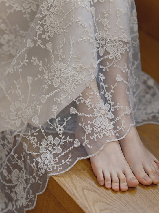 Close-up of sheer embroidered lace hem draped over bare feet, highlighting delicate floral details and soft fairycore elegance.