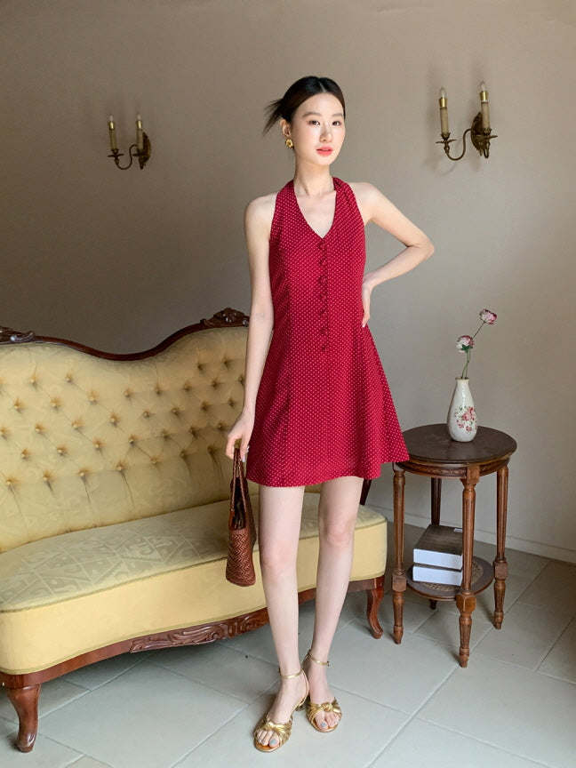 Full-length shot of a woman in a red polka dot halter  short dress, styled with gold sandals and a brown woven bag for a romantic princesscore look.