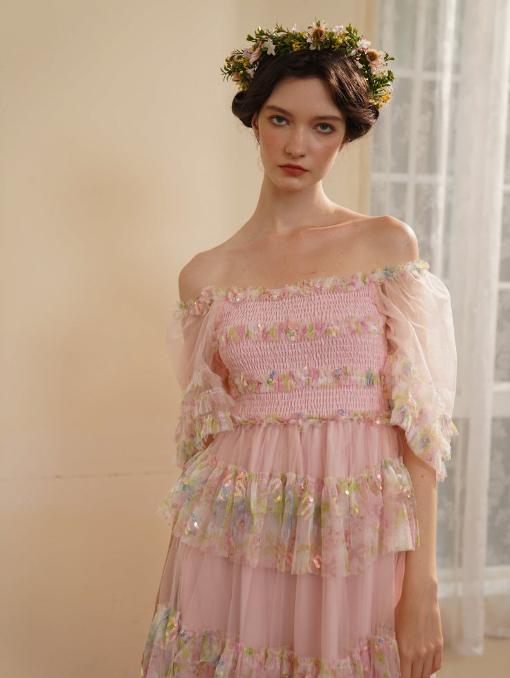 A woman wearing a floral crown gazes softly in a pink off-shoulder ruffle dress, embodying a delicate and enchanting fairycore look.