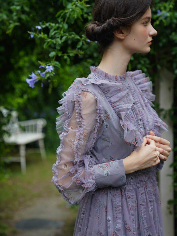 Side view of a model in a soft lavender ruffle dress, hands gently clasped, evoking a quiet vintage elegance in a fairytale garden.