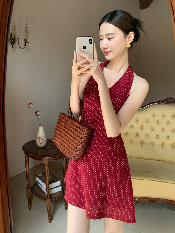 Woman taking a mirror selfie in a red halter mini dress with white dots, styled in a feminine fairycore outfit with a brown woven bag.
