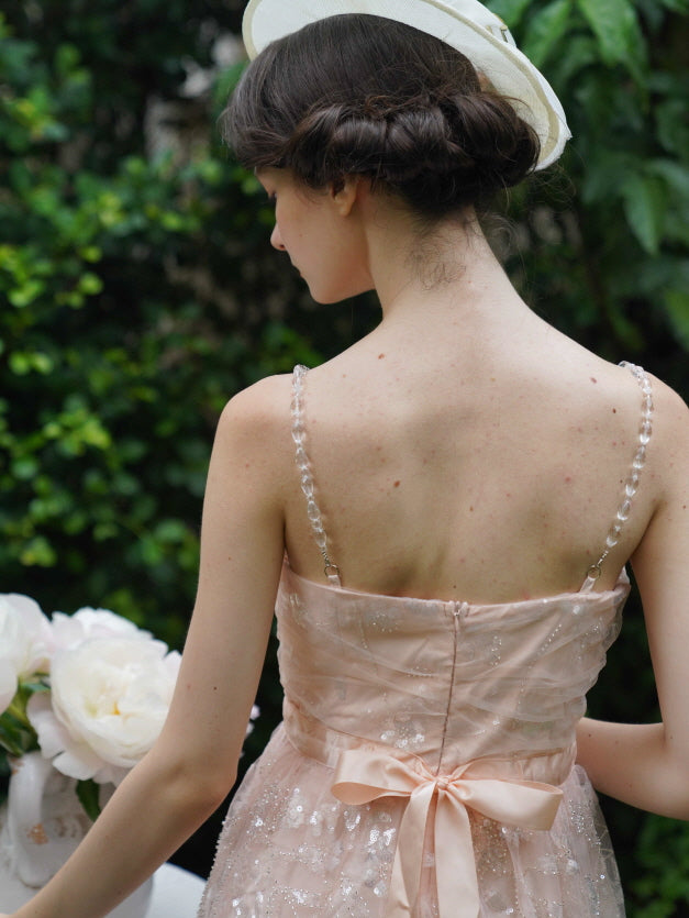 Back view of a blush pink dress with pearl straps and a satin ribbon bow, styled with a garden hat for a delicate and dreamy princesscore look.