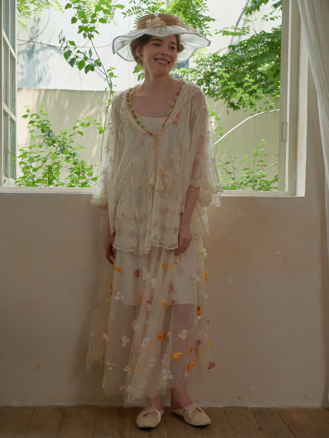 Wearing a lace-trimmed poncho layered over a dreamy flower-embellished mesh dress, the model smiles in a vintage-inspired spring look.