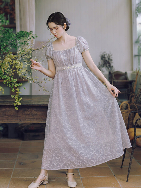 Wearing a lavender vintage dress with floral textures, a woman gently lifts her skirt while surrounded by botanical vintage decor.
