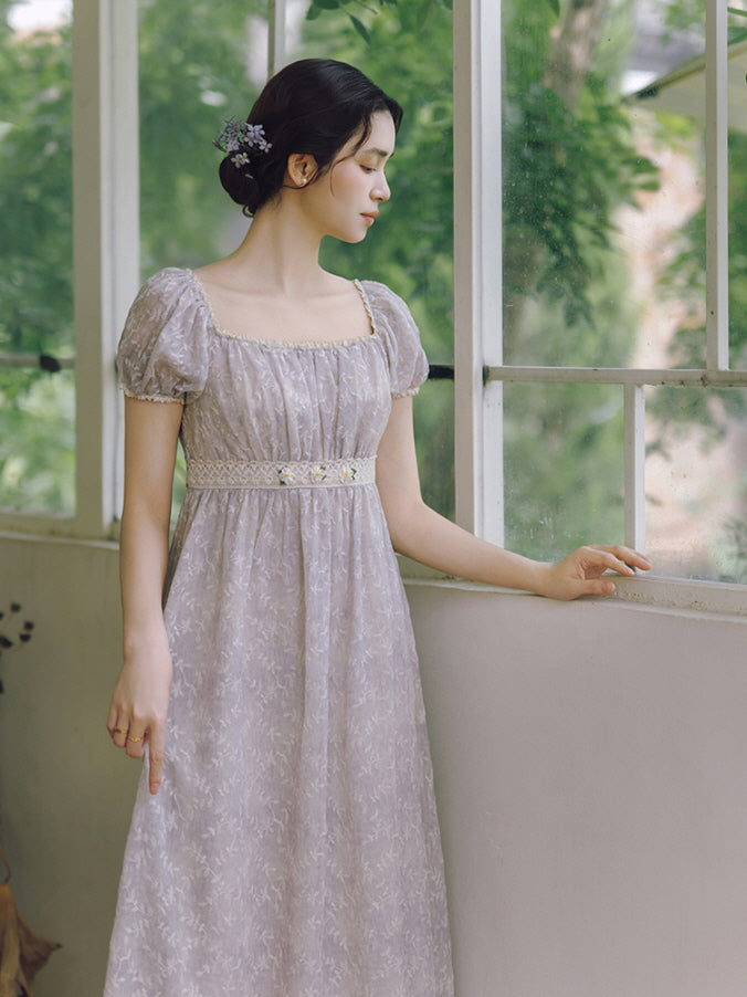 A woman in a lavender fairytale dress with puff sleeves gazes out the window, wrapped in soft light and vintage cottagecore serenity.