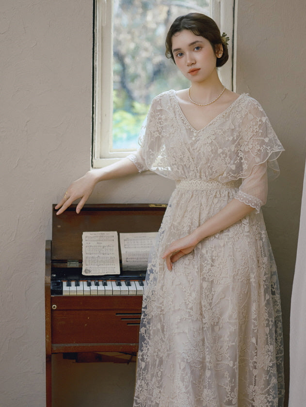 A woman in a vintage ivory lace dress stands beside a piano under natural light, embodying a timeless and romantic cottagecore look.