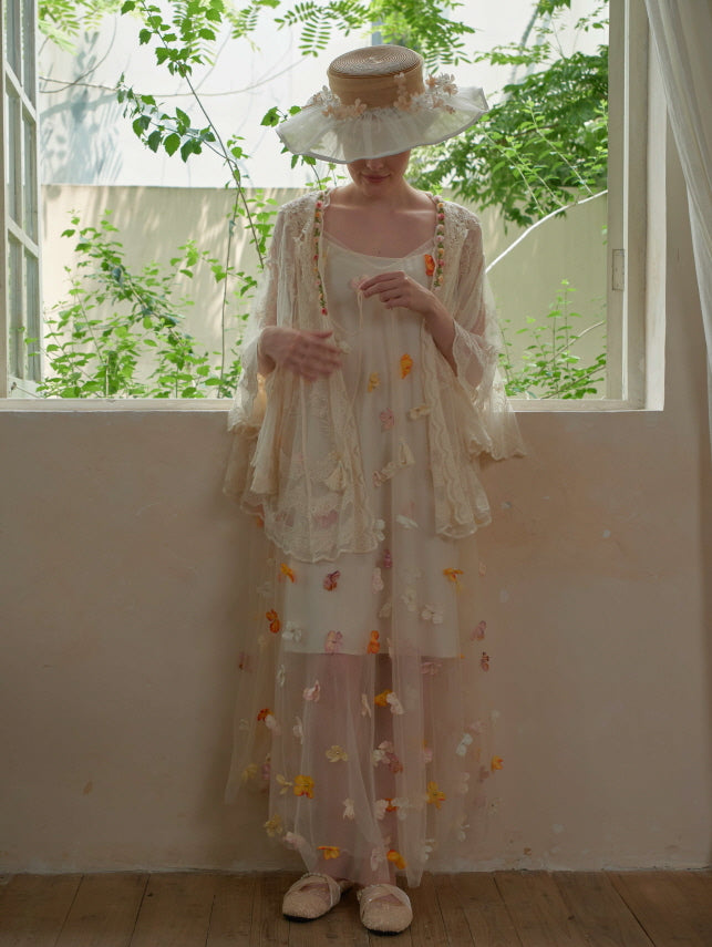 The model gently looks down while wearing a floral mesh dress layered with a lace poncho, creating a serene fairytale-inspired fairycore look.
