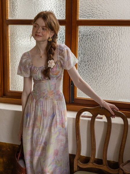 A woman stands by a textured glass window, wearing a pastel floral dress with puff sleeves, radiating a soft, vintage-inspired cottagecore charm.