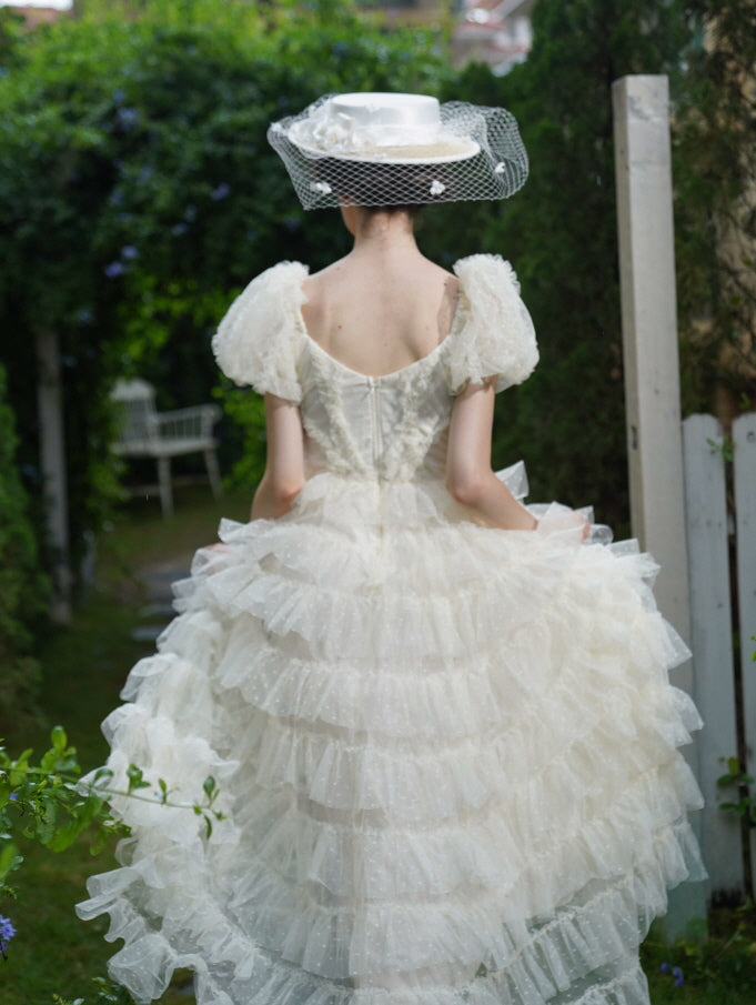 Back view of an ivory ruffled dress with a romantic silhouette, as the model walks through lush greenery in a soft princesscore atmosphere.