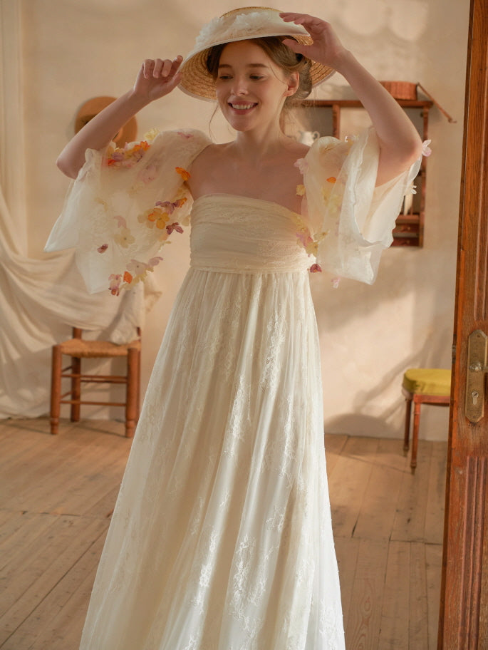 She playfully adjusts her floral hat while wearing a flowy lace gown with sheer 3D petal sleeves, perfect for a fairytale aesthetic.