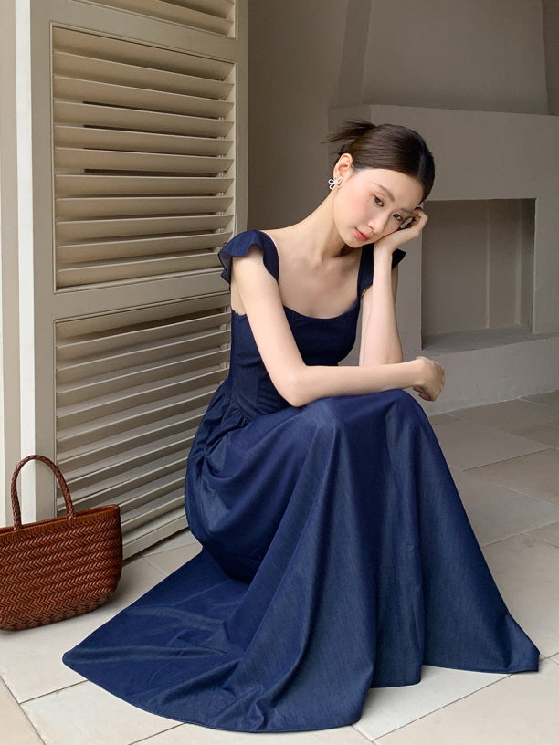 Wearing a navy fairytale dress, a woman sits quietly by the shuttered window with a soft expression, exuding timeless princesscore elegance.