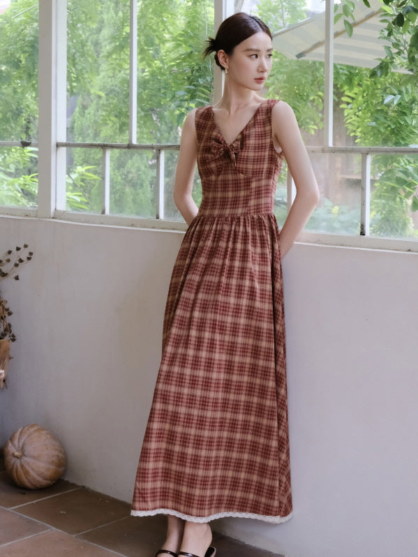 A woman stands by a large window in a red plaid vintage dress with a ribbon detail, surrounded by greenery and soft cottagecore lighting.