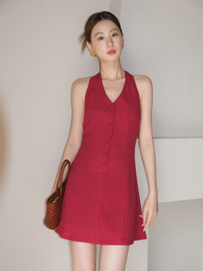 Model poses in a cherry red polka dot halter short dress holding a woven bag, styled with subtle elegance for a summer party outfit.