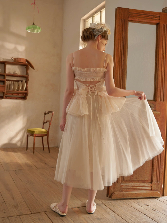 The model turns slightly while lifting the soft tulle skirt of a cream two-piece dress with lace-up back detail, styled in a romantic fairycore look.