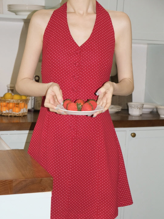 Close-up of a red halter polka dot dress with a flared silhouette, as the model gently holds a plate of strawberries in a cozy cottage kitchen.