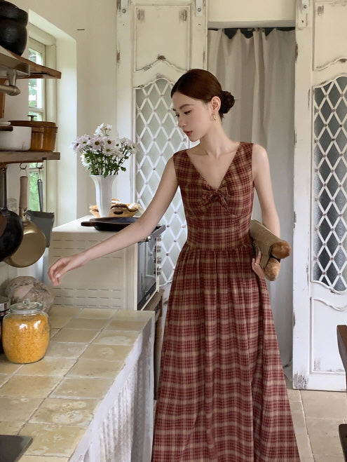 In a vintage kitchen, a woman in a red plaid cottagecore dress with a bow bodice reaches for a jar, holding a fresh baguette in her arm.
