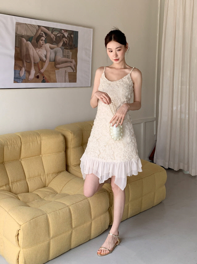 A woman holds a pearl bag while wearing a floral-textured ivory mini dress with a layered chiffon hem, styled in a soft coquette aesthetic.