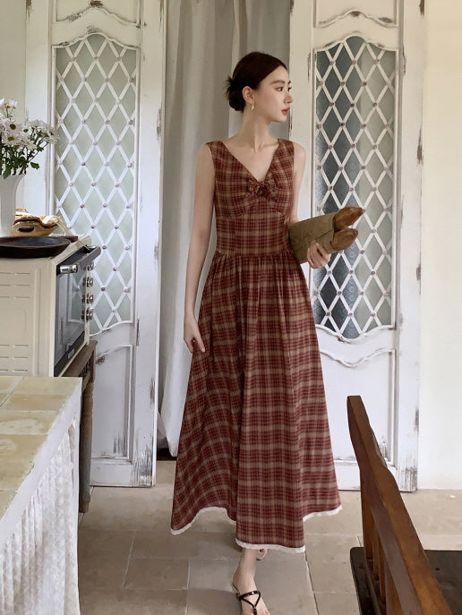 A woman walks gracefully through a rustic doorway in a sleeveless check dress, carrying bread and evoking a romantic countryside lifestyle.