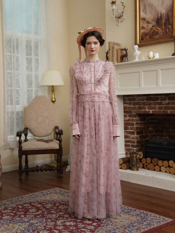 The model stands in a soft pink floral dress with sheer ruffles and long sleeves, evoking timeless elegance in a vintage-inspired room.