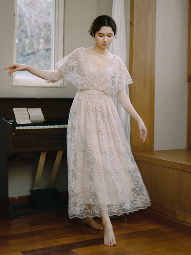 A woman twirls gracefully in a vintage-inspired lace dress, barefoot on a wooden floor, evoking a fairytale and cottagecore atmosphere.