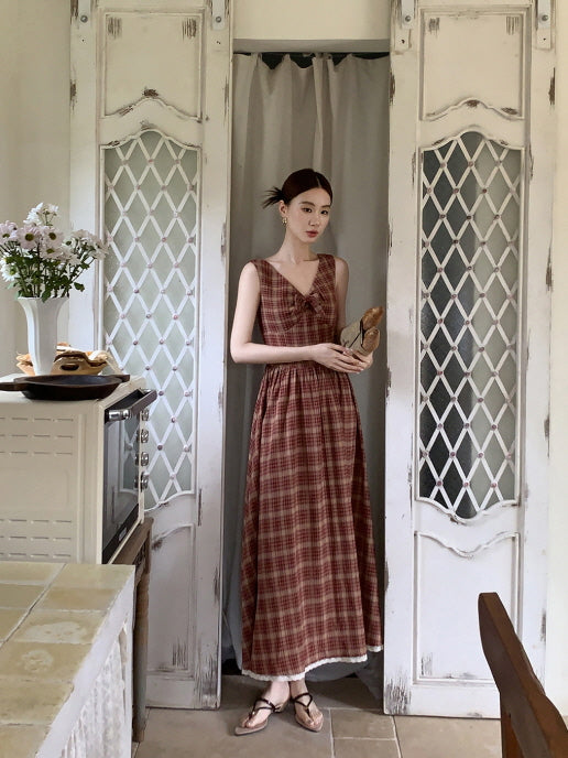 A woman in a red plaid dress stands in a vintage kitchen doorway, holding a baguette and embodying a quiet romantic countryside charm.