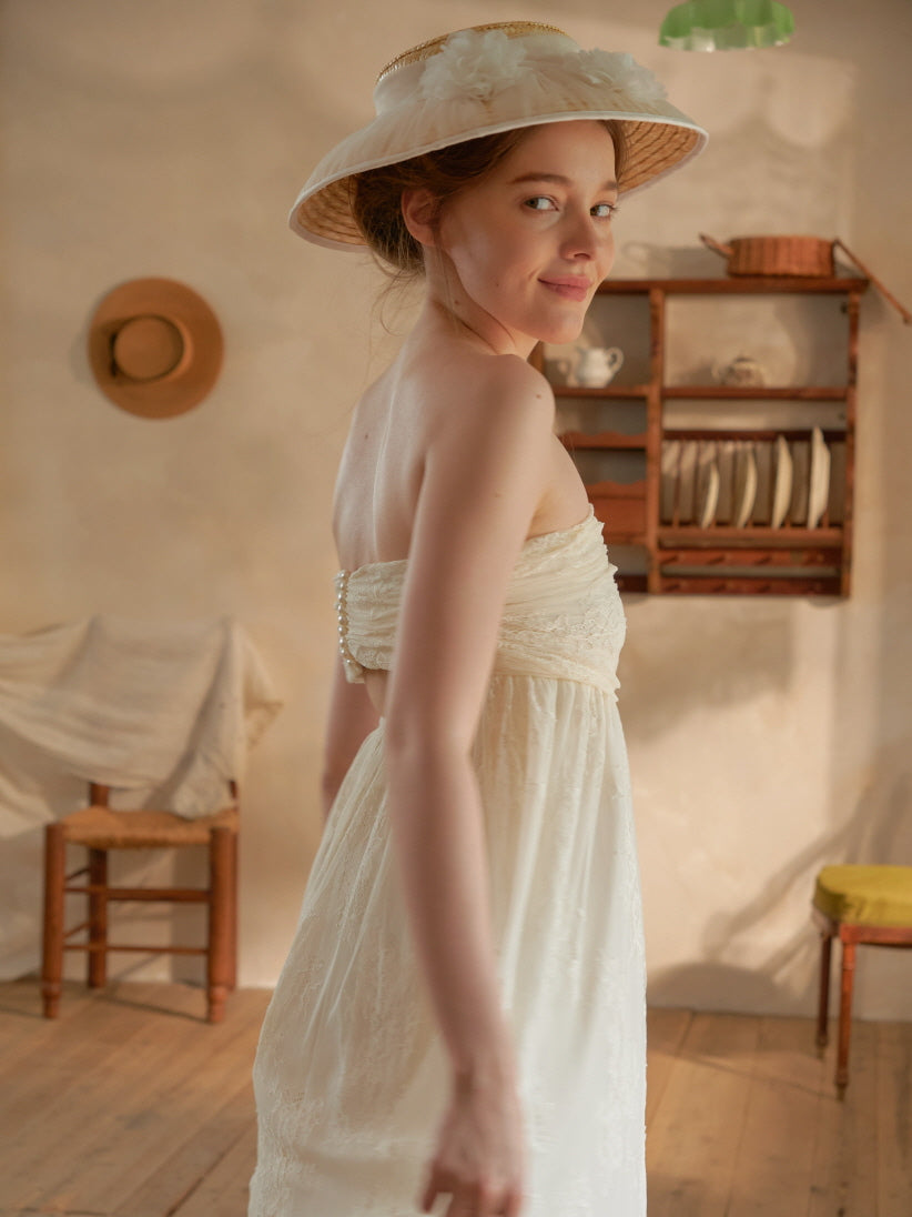 She looks over her shoulder in a romantic backless lace dress, styled with a soft hat for a vintage-inspired fairytale aesthetic.