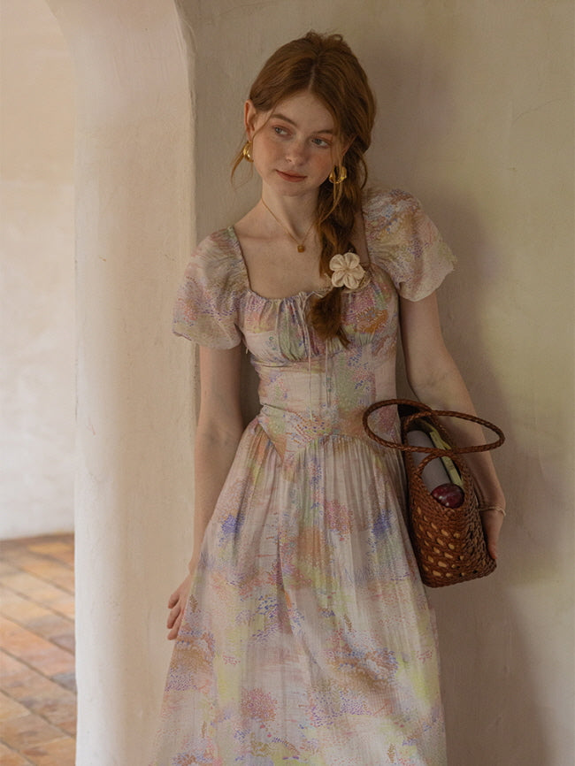 A woman leans against a rustic archway, holding a woven bag filled with fruits while wearing a pastel floral dress with puff sleeves, evoking a soft, cottagecore aesthetic.