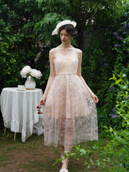 Full-length view of a model in a blush layered dress with sheer overlay, standing in a blooming garden for a light and graceful princesscore look.