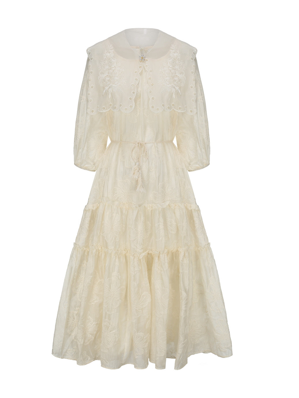 Front view of a cream embroidered tiered dress with a scalloped capelet and drawstring waist, styled for a romantic vintage aesthetic.