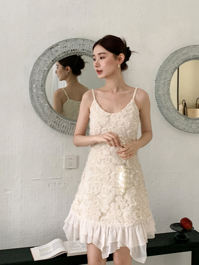 In front of a round mirror, a woman stands in a romantic cream mini dress with layered hem and rosette detailing, evoking a soft fairycore mood.