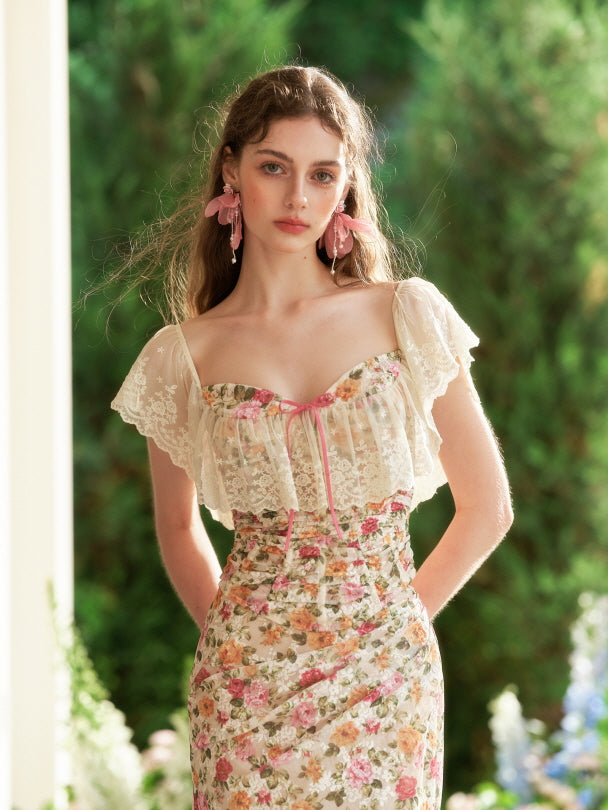 The model gazes softly while wearing a fairytale-inspired floral corset dress with sheer ruffled sleeves and a delicate pink ribbon neckline.