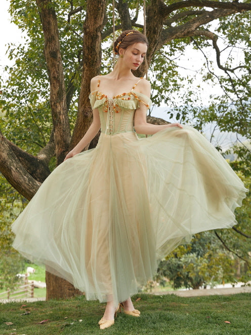 A woman poses gracefully in a soft green princesscore gown, lifting the tulle skirt to reveal its romantic volume and fairytale charm.
