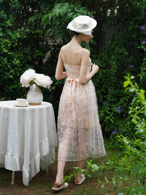 Model rests her hand on a lace tea table, wearing a blush sequin dress with sheer puff sleeves draped off-shoulder for a romantic fairycore vibe.
