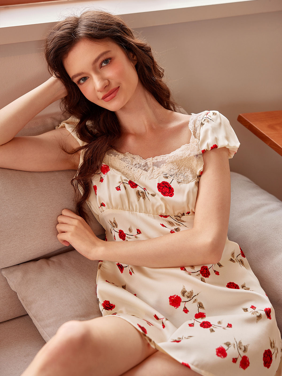Smiling softly on a sofa, the model wears a romantic floral nightdress with lace trim, capturing a sweet and relaxed coquette aesthetic.